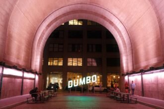 A lit archway leads to the dumbo sign at night.