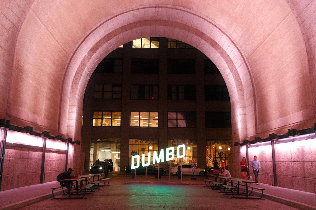 A lit archway leads to the dumbo sign at night.